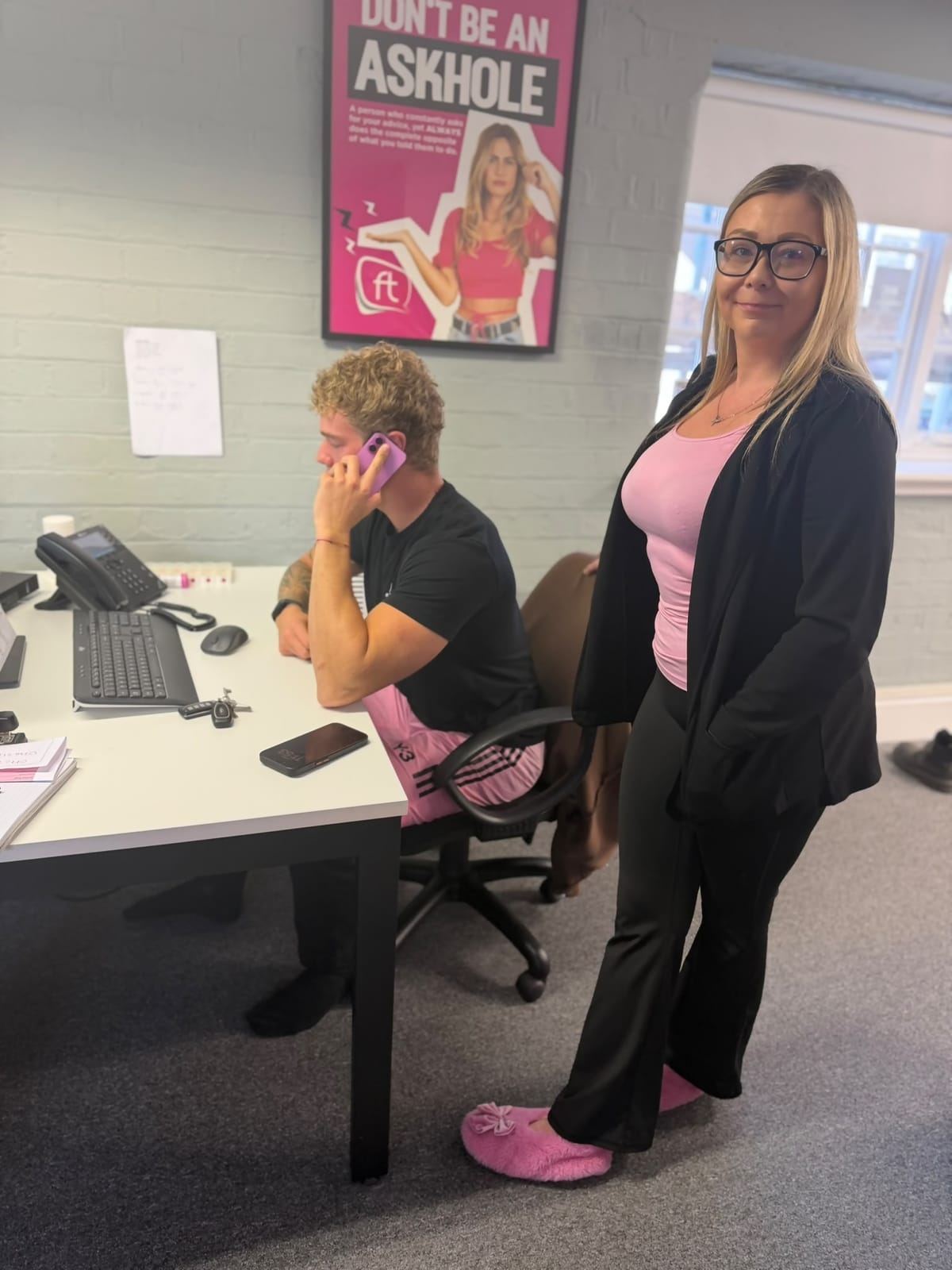 FT Recruitment team member in a pink top and pink slippers standing next to a colleague on the phone